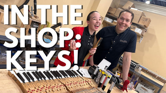 Brigham Larson stands next to one of his technicians, Ezzy. They post behind a table of piano keys being worked on. Title reads "In The Shop: Keys!"